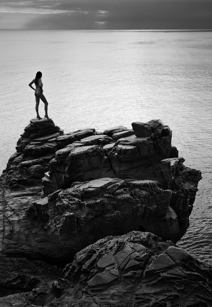 woman stands on rock above sea